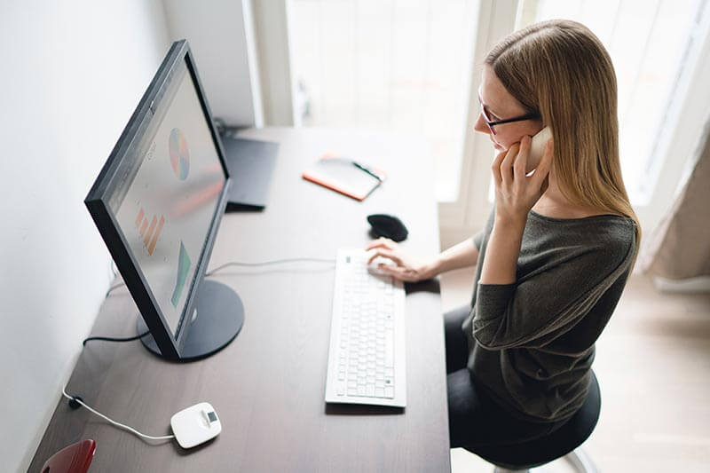 Woman on mobile device working from home on desktop