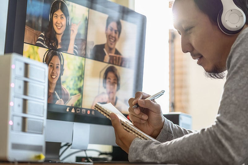 man hand-writing notebook during video conference call
